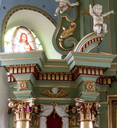 Zdjęcie nr 4: Ołtarz przyścienny, architektoniczny, trójosiowy, dwukondygnacyjny ze zwieńczeniem. Nastawa umieszczona na wysokim, dwudzielnym cokole w górnej części zdobionym na przemian dekoracją płycinową i motywem muszli palmetowej z podwieszoną girlandą kwiatową oraz rozetkami. Cokół wieńczy profilowany gzyms dekorowany kostkowaniem. Antepedium współczesne, marmurowe z umieszczonym centralnie prostym, równoramiennym krzyżem. Na mensie ustawione tabernakulum z tronem wystawienia, o formach architektonicznych, ujęte zdwojonymi, smukłymi kolumienkami o złoconych trzonach umieszczonymi na wysokich cokołach. Podpory dźwigają odcinki pełnego belkowania, na których ustawione złocone figury klęczących aniołów. Część centralna o linii wypukłej, dwukondygnacyjna. W kondygnacji pierwszej złocone drzwiczki z płaskorzeźbionym kielichem z hostią na tle glorii promienistej, powyżej, w kondygnacji drugiej tron wystawienia ujęty rzeźbioną, złoconą kotarą. W zwieńczeniu srebrzona figura baranka apokaliptycznego leżącego na księdze. Nastawa ujęta zdwojonymi, kompozytowymi kolumnami o złoconych trzonach i kapitelach. Pomiędzy kolumnami, w niszach rzeźbione figury św. Piotra (z lewej) i św. Pawła (z prawej), ponad którymi motyw symetrycznie podwieszonej kotary. Kolumny dźwigają odcinki pełnego belkowania z fryzem dekorowanym rozetkami i uskrzydlonymi główkami anielskimi oraz wydatnym gzymsem dekorowanym kostkowaniem. Na osi wewnętrznej pary komun dodatkowo ustawione odcinki półkolistego tympanonu, na których siedzą putta. W polu głównym ołtarza złocona, profilowana rama w kształcie stojącego prostokąta zamkniętego łukiem nadwieszonym mieszcząca barokowy obraz Matki Boskiej z Dzieciątkiem. Nieco powyżej, w osi ołtarza dwa putta unoszące złoconą koronę typu zamkniętego zwieńczoną krzyżem. Kondygnacja druga ujęta parą pilastrów o kompozytowych kapitelach oraz uszami w formie spływów wolutowych, na których siedzące putta. W polu złocona i profilowana rama w kształcie stojącego prostokąta mieszcząca obraz przedstawiający Trójcę Świętą. Całość ołtarza wieńczy profilowany gzyms dekorowany kostkowaniem i zamknięty niskim, trójkątnym przyczółkiem. W polu tympanonu uskrzydlona główka anielska. Struktura ołtarza polichromowana w kolorze jasnozielonym z elementami czerwieni i bieli. Detale architektoniczne, ornamenty oraz szaty postaci złocone.

