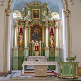 Zdjęcie nr 1: Ołtarz przyścienny, architektoniczny, trójosiowy, dwukondygnacyjny ze zwieńczeniem. Nastawa umieszczona na wysokim, dwudzielnym cokole w górnej części zdobionym na przemian dekoracją płycinową i motywem muszli palmetowej z podwieszoną girlandą kwiatową oraz rozetkami. Cokół wieńczy profilowany gzyms dekorowany kostkowaniem. Antepedium współczesne, marmurowe z umieszczonym centralnie prostym, równoramiennym krzyżem. Na mensie ustawione tabernakulum z tronem wystawienia, o formach architektonicznych, ujęte zdwojonymi, smukłymi kolumienkami o złoconych trzonach umieszczonymi na wysokich cokołach. Podpory dźwigają odcinki pełnego belkowania, na których ustawione złocone figury klęczących aniołów. Część centralna o linii wypukłej, dwukondygnacyjna. W kondygnacji pierwszej złocone drzwiczki z płaskorzeźbionym kielichem z hostią na tle glorii promienistej, powyżej, w kondygnacji drugiej tron wystawienia ujęty rzeźbioną, złoconą kotarą. W zwieńczeniu srebrzona figura baranka apokaliptycznego leżącego na księdze. Nastawa ujęta zdwojonymi, kompozytowymi kolumnami o złoconych trzonach i kapitelach. Pomiędzy kolumnami, w niszach rzeźbione figury św. Piotra (z lewej) i św. Pawła (z prawej), ponad którymi motyw symetrycznie podwieszonej kotary. Kolumny dźwigają odcinki pełnego belkowania z fryzem dekorowanym rozetkami i uskrzydlonymi główkami anielskimi oraz wydatnym gzymsem dekorowanym kostkowaniem. Na osi wewnętrznej pary komun dodatkowo ustawione odcinki półkolistego tympanonu, na których siedzą putta. W polu głównym ołtarza złocona, profilowana rama w kształcie stojącego prostokąta zamkniętego łukiem nadwieszonym mieszcząca barokowy obraz Matki Boskiej z Dzieciątkiem. Nieco powyżej, w osi ołtarza dwa putta unoszące złoconą koronę typu zamkniętego zwieńczoną krzyżem. Kondygnacja druga ujęta parą pilastrów o kompozytowych kapitelach oraz uszami w formie spływów wolutowych, na których siedzące putta. W polu złocona i profilowana rama w kształcie stojącego prostokąta mieszcząca obraz przedstawiający Trójcę Świętą. Całość ołtarza wieńczy profilowany gzyms dekorowany kostkowaniem i zamknięty niskim, trójkątnym przyczółkiem. W polu tympanonu uskrzydlona główka anielska. Struktura ołtarza polichromowana w kolorze jasnozielonym z elementami czerwieni i bieli. Detale architektoniczne, ornamenty oraz szaty postaci złocone.

