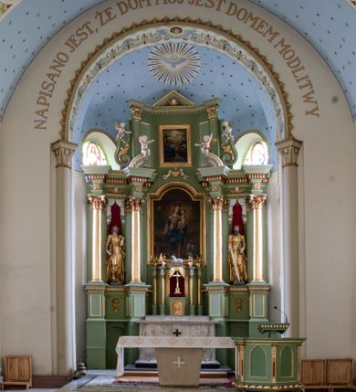 Zdjęcie nr 2: Ołtarz przyścienny, architektoniczny, trójosiowy, dwukondygnacyjny ze zwieńczeniem. Nastawa umieszczona na wysokim, dwudzielnym cokole w górnej części zdobionym na przemian dekoracją płycinową i motywem muszli palmetowej z podwieszoną girlandą kwiatową oraz rozetkami. Cokół wieńczy profilowany gzyms dekorowany kostkowaniem. Antepedium współczesne, marmurowe z umieszczonym centralnie prostym, równoramiennym krzyżem. Na mensie ustawione tabernakulum z tronem wystawienia, o formach architektonicznych, ujęte zdwojonymi, smukłymi kolumienkami o złoconych trzonach umieszczonymi na wysokich cokołach. Podpory dźwigają odcinki pełnego belkowania, na których ustawione złocone figury klęczących aniołów. Część centralna o linii wypukłej, dwukondygnacyjna. W kondygnacji pierwszej złocone drzwiczki z płaskorzeźbionym kielichem z hostią na tle glorii promienistej, powyżej, w kondygnacji drugiej tron wystawienia ujęty rzeźbioną, złoconą kotarą. W zwieńczeniu srebrzona figura baranka apokaliptycznego leżącego na księdze. Nastawa ujęta zdwojonymi, kompozytowymi kolumnami o złoconych trzonach i kapitelach. Pomiędzy kolumnami, w niszach rzeźbione figury św. Piotra (z lewej) i św. Pawła (z prawej), ponad którymi motyw symetrycznie podwieszonej kotary. Kolumny dźwigają odcinki pełnego belkowania z fryzem dekorowanym rozetkami i uskrzydlonymi główkami anielskimi oraz wydatnym gzymsem dekorowanym kostkowaniem. Na osi wewnętrznej pary komun dodatkowo ustawione odcinki półkolistego tympanonu, na których siedzą putta. W polu głównym ołtarza złocona, profilowana rama w kształcie stojącego prostokąta zamkniętego łukiem nadwieszonym mieszcząca barokowy obraz Matki Boskiej z Dzieciątkiem. Nieco powyżej, w osi ołtarza dwa putta unoszące złoconą koronę typu zamkniętego zwieńczoną krzyżem. Kondygnacja druga ujęta parą pilastrów o kompozytowych kapitelach oraz uszami w formie spływów wolutowych, na których siedzące putta. W polu złocona i profilowana rama w kształcie stojącego prostokąta mieszcząca obraz przedstawiający Trójcę Świętą. Całość ołtarza wieńczy profilowany gzyms dekorowany kostkowaniem i zamknięty niskim, trójkątnym przyczółkiem. W polu tympanonu uskrzydlona główka anielska. Struktura ołtarza polichromowana w kolorze jasnozielonym z elementami czerwieni i bieli. Detale architektoniczne, ornamenty oraz szaty postaci złocone.

