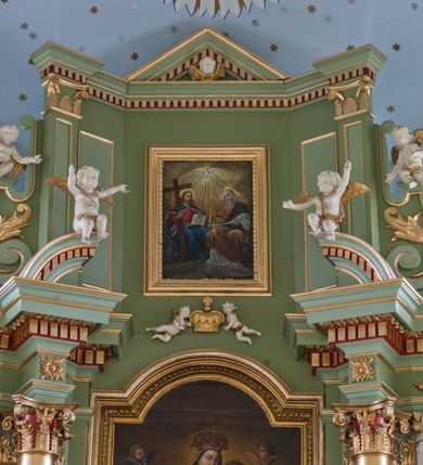 Zdjęcie nr 11: Ołtarz przyścienny, architektoniczny, trójosiowy, dwukondygnacyjny ze zwieńczeniem. Nastawa umieszczona na wysokim, dwudzielnym cokole w górnej części zdobionym na przemian dekoracją płycinową i motywem muszli palmetowej z podwieszoną girlandą kwiatową oraz rozetkami. Cokół wieńczy profilowany gzyms dekorowany kostkowaniem. Antepedium współczesne, marmurowe z umieszczonym centralnie prostym, równoramiennym krzyżem. Na mensie ustawione tabernakulum z tronem wystawienia, o formach architektonicznych, ujęte zdwojonymi, smukłymi kolumienkami o złoconych trzonach umieszczonymi na wysokich cokołach. Podpory dźwigają odcinki pełnego belkowania, na których ustawione złocone figury klęczących aniołów. Część centralna o linii wypukłej, dwukondygnacyjna. W kondygnacji pierwszej złocone drzwiczki z płaskorzeźbionym kielichem z hostią na tle glorii promienistej, powyżej, w kondygnacji drugiej tron wystawienia ujęty rzeźbioną, złoconą kotarą. W zwieńczeniu srebrzona figura baranka apokaliptycznego leżącego na księdze. Nastawa ujęta zdwojonymi, kompozytowymi kolumnami o złoconych trzonach i kapitelach. Pomiędzy kolumnami, w niszach rzeźbione figury św. Piotra (z lewej) i św. Pawła (z prawej), ponad którymi motyw symetrycznie podwieszonej kotary. Kolumny dźwigają odcinki pełnego belkowania z fryzem dekorowanym rozetkami i uskrzydlonymi główkami anielskimi oraz wydatnym gzymsem dekorowanym kostkowaniem. Na osi wewnętrznej pary komun dodatkowo ustawione odcinki półkolistego tympanonu, na których siedzą putta. W polu głównym ołtarza złocona, profilowana rama w kształcie stojącego prostokąta zamkniętego łukiem nadwieszonym mieszcząca barokowy obraz Matki Boskiej z Dzieciątkiem. Nieco powyżej, w osi ołtarza dwa putta unoszące złoconą koronę typu zamkniętego zwieńczoną krzyżem. Kondygnacja druga ujęta parą pilastrów o kompozytowych kapitelach oraz uszami w formie spływów wolutowych, na których siedzące putta. W polu złocona i profilowana rama w kształcie stojącego prostokąta mieszcząca obraz przedstawiający Trójcę Świętą. Całość ołtarza wieńczy profilowany gzyms dekorowany kostkowaniem i zamknięty niskim, trójkątnym przyczółkiem. W polu tympanonu uskrzydlona główka anielska. Struktura ołtarza polichromowana w kolorze jasnozielonym z elementami czerwieni i bieli. Detale architektoniczne, ornamenty oraz szaty postaci złocone.

