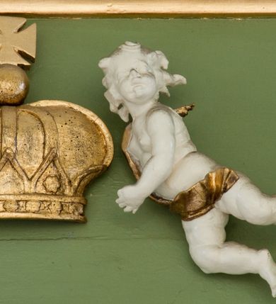 Zdjęcie nr 24: Ołtarz przyścienny, architektoniczny, trójosiowy, dwukondygnacyjny ze zwieńczeniem. Nastawa umieszczona na wysokim, dwudzielnym cokole w górnej części zdobionym na przemian dekoracją płycinową i motywem muszli palmetowej z podwieszoną girlandą kwiatową oraz rozetkami. Cokół wieńczy profilowany gzyms dekorowany kostkowaniem. Antepedium współczesne, marmurowe z umieszczonym centralnie prostym, równoramiennym krzyżem. Na mensie ustawione tabernakulum z tronem wystawienia, o formach architektonicznych, ujęte zdwojonymi, smukłymi kolumienkami o złoconych trzonach umieszczonymi na wysokich cokołach. Podpory dźwigają odcinki pełnego belkowania, na których ustawione złocone figury klęczących aniołów. Część centralna o linii wypukłej, dwukondygnacyjna. W kondygnacji pierwszej złocone drzwiczki z płaskorzeźbionym kielichem z hostią na tle glorii promienistej, powyżej, w kondygnacji drugiej tron wystawienia ujęty rzeźbioną, złoconą kotarą. W zwieńczeniu srebrzona figura baranka apokaliptycznego leżącego na księdze. Nastawa ujęta zdwojonymi, kompozytowymi kolumnami o złoconych trzonach i kapitelach. Pomiędzy kolumnami, w niszach rzeźbione figury św. Piotra (z lewej) i św. Pawła (z prawej), ponad którymi motyw symetrycznie podwieszonej kotary. Kolumny dźwigają odcinki pełnego belkowania z fryzem dekorowanym rozetkami i uskrzydlonymi główkami anielskimi oraz wydatnym gzymsem dekorowanym kostkowaniem. Na osi wewnętrznej pary komun dodatkowo ustawione odcinki półkolistego tympanonu, na których siedzą putta. W polu głównym ołtarza złocona, profilowana rama w kształcie stojącego prostokąta zamkniętego łukiem nadwieszonym mieszcząca barokowy obraz Matki Boskiej z Dzieciątkiem. Nieco powyżej, w osi ołtarza dwa putta unoszące złoconą koronę typu zamkniętego zwieńczoną krzyżem. Kondygnacja druga ujęta parą pilastrów o kompozytowych kapitelach oraz uszami w formie spływów wolutowych, na których siedzące putta. W polu złocona i profilowana rama w kształcie stojącego prostokąta mieszcząca obraz przedstawiający Trójcę Świętą. Całość ołtarza wieńczy profilowany gzyms dekorowany kostkowaniem i zamknięty niskim, trójkątnym przyczółkiem. W polu tympanonu uskrzydlona główka anielska. Struktura ołtarza polichromowana w kolorze jasnozielonym z elementami czerwieni i bieli. Detale architektoniczne, ornamenty oraz szaty postaci złocone.

