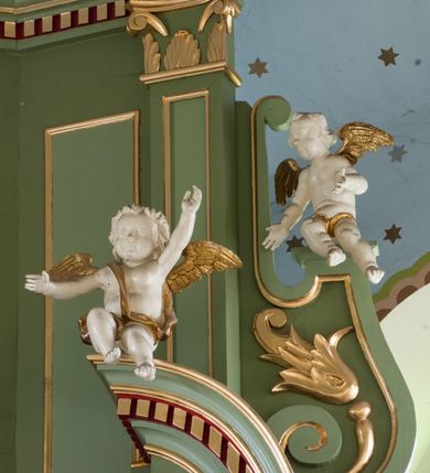 Zdjęcie nr 15: Ołtarz przyścienny, architektoniczny, trójosiowy, dwukondygnacyjny ze zwieńczeniem. Nastawa umieszczona na wysokim, dwudzielnym cokole w górnej części zdobionym na przemian dekoracją płycinową i motywem muszli palmetowej z podwieszoną girlandą kwiatową oraz rozetkami. Cokół wieńczy profilowany gzyms dekorowany kostkowaniem. Antepedium współczesne, marmurowe z umieszczonym centralnie prostym, równoramiennym krzyżem. Na mensie ustawione tabernakulum z tronem wystawienia, o formach architektonicznych, ujęte zdwojonymi, smukłymi kolumienkami o złoconych trzonach umieszczonymi na wysokich cokołach. Podpory dźwigają odcinki pełnego belkowania, na których ustawione złocone figury klęczących aniołów. Część centralna o linii wypukłej, dwukondygnacyjna. W kondygnacji pierwszej złocone drzwiczki z płaskorzeźbionym kielichem z hostią na tle glorii promienistej, powyżej, w kondygnacji drugiej tron wystawienia ujęty rzeźbioną, złoconą kotarą. W zwieńczeniu srebrzona figura baranka apokaliptycznego leżącego na księdze. Nastawa ujęta zdwojonymi, kompozytowymi kolumnami o złoconych trzonach i kapitelach. Pomiędzy kolumnami, w niszach rzeźbione figury św. Piotra (z lewej) i św. Pawła (z prawej), ponad którymi motyw symetrycznie podwieszonej kotary. Kolumny dźwigają odcinki pełnego belkowania z fryzem dekorowanym rozetkami i uskrzydlonymi główkami anielskimi oraz wydatnym gzymsem dekorowanym kostkowaniem. Na osi wewnętrznej pary komun dodatkowo ustawione odcinki półkolistego tympanonu, na których siedzą putta. W polu głównym ołtarza złocona, profilowana rama w kształcie stojącego prostokąta zamkniętego łukiem nadwieszonym mieszcząca barokowy obraz Matki Boskiej z Dzieciątkiem. Nieco powyżej, w osi ołtarza dwa putta unoszące złoconą koronę typu zamkniętego zwieńczoną krzyżem. Kondygnacja druga ujęta parą pilastrów o kompozytowych kapitelach oraz uszami w formie spływów wolutowych, na których siedzące putta. W polu złocona i profilowana rama w kształcie stojącego prostokąta mieszcząca obraz przedstawiający Trójcę Świętą. Całość ołtarza wieńczy profilowany gzyms dekorowany kostkowaniem i zamknięty niskim, trójkątnym przyczółkiem. W polu tympanonu uskrzydlona główka anielska. Struktura ołtarza polichromowana w kolorze jasnozielonym z elementami czerwieni i bieli. Detale architektoniczne, ornamenty oraz szaty postaci złocone.

