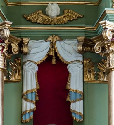 Zdjęcie nr 13: Ołtarz przyścienny, architektoniczny, trójosiowy, dwukondygnacyjny ze zwieńczeniem. Nastawa umieszczona na wysokim, dwudzielnym cokole w górnej części zdobionym na przemian dekoracją płycinową i motywem muszli palmetowej z podwieszoną girlandą kwiatową oraz rozetkami. Cokół wieńczy profilowany gzyms dekorowany kostkowaniem. Antepedium współczesne, marmurowe z umieszczonym centralnie prostym, równoramiennym krzyżem. Na mensie ustawione tabernakulum z tronem wystawienia, o formach architektonicznych, ujęte zdwojonymi, smukłymi kolumienkami o złoconych trzonach umieszczonymi na wysokich cokołach. Podpory dźwigają odcinki pełnego belkowania, na których ustawione złocone figury klęczących aniołów. Część centralna o linii wypukłej, dwukondygnacyjna. W kondygnacji pierwszej złocone drzwiczki z płaskorzeźbionym kielichem z hostią na tle glorii promienistej, powyżej, w kondygnacji drugiej tron wystawienia ujęty rzeźbioną, złoconą kotarą. W zwieńczeniu srebrzona figura baranka apokaliptycznego leżącego na księdze. Nastawa ujęta zdwojonymi, kompozytowymi kolumnami o złoconych trzonach i kapitelach. Pomiędzy kolumnami, w niszach rzeźbione figury św. Piotra (z lewej) i św. Pawła (z prawej), ponad którymi motyw symetrycznie podwieszonej kotary. Kolumny dźwigają odcinki pełnego belkowania z fryzem dekorowanym rozetkami i uskrzydlonymi główkami anielskimi oraz wydatnym gzymsem dekorowanym kostkowaniem. Na osi wewnętrznej pary komun dodatkowo ustawione odcinki półkolistego tympanonu, na których siedzą putta. W polu głównym ołtarza złocona, profilowana rama w kształcie stojącego prostokąta zamkniętego łukiem nadwieszonym mieszcząca barokowy obraz Matki Boskiej z Dzieciątkiem. Nieco powyżej, w osi ołtarza dwa putta unoszące złoconą koronę typu zamkniętego zwieńczoną krzyżem. Kondygnacja druga ujęta parą pilastrów o kompozytowych kapitelach oraz uszami w formie spływów wolutowych, na których siedzące putta. W polu złocona i profilowana rama w kształcie stojącego prostokąta mieszcząca obraz przedstawiający Trójcę Świętą. Całość ołtarza wieńczy profilowany gzyms dekorowany kostkowaniem i zamknięty niskim, trójkątnym przyczółkiem. W polu tympanonu uskrzydlona główka anielska. Struktura ołtarza polichromowana w kolorze jasnozielonym z elementami czerwieni i bieli. Detale architektoniczne, ornamenty oraz szaty postaci złocone.

