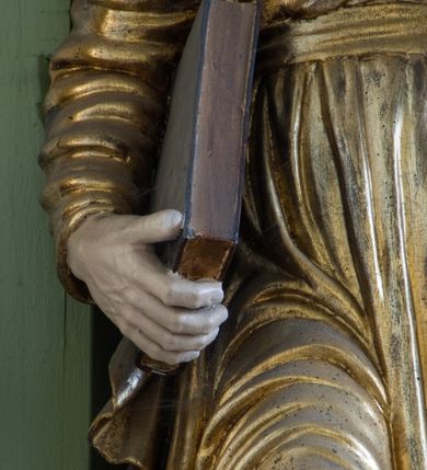 Zdjęcie nr 34: Ołtarz przyścienny, architektoniczny, trójosiowy, dwukondygnacyjny ze zwieńczeniem. Nastawa umieszczona na wysokim, dwudzielnym cokole w górnej części zdobionym na przemian dekoracją płycinową i motywem muszli palmetowej z podwieszoną girlandą kwiatową oraz rozetkami. Cokół wieńczy profilowany gzyms dekorowany kostkowaniem. Antepedium współczesne, marmurowe z umieszczonym centralnie prostym, równoramiennym krzyżem. Na mensie ustawione tabernakulum z tronem wystawienia, o formach architektonicznych, ujęte zdwojonymi, smukłymi kolumienkami o złoconych trzonach umieszczonymi na wysokich cokołach. Podpory dźwigają odcinki pełnego belkowania, na których ustawione złocone figury klęczących aniołów. Część centralna o linii wypukłej, dwukondygnacyjna. W kondygnacji pierwszej złocone drzwiczki z płaskorzeźbionym kielichem z hostią na tle glorii promienistej, powyżej, w kondygnacji drugiej tron wystawienia ujęty rzeźbioną, złoconą kotarą. W zwieńczeniu srebrzona figura baranka apokaliptycznego leżącego na księdze. Nastawa ujęta zdwojonymi, kompozytowymi kolumnami o złoconych trzonach i kapitelach. Pomiędzy kolumnami, w niszach rzeźbione figury św. Piotra (z lewej) i św. Pawła (z prawej), ponad którymi motyw symetrycznie podwieszonej kotary. Kolumny dźwigają odcinki pełnego belkowania z fryzem dekorowanym rozetkami i uskrzydlonymi główkami anielskimi oraz wydatnym gzymsem dekorowanym kostkowaniem. Na osi wewnętrznej pary komun dodatkowo ustawione odcinki półkolistego tympanonu, na których siedzą putta. W polu głównym ołtarza złocona, profilowana rama w kształcie stojącego prostokąta zamkniętego łukiem nadwieszonym mieszcząca barokowy obraz Matki Boskiej z Dzieciątkiem. Nieco powyżej, w osi ołtarza dwa putta unoszące złoconą koronę typu zamkniętego zwieńczoną krzyżem. Kondygnacja druga ujęta parą pilastrów o kompozytowych kapitelach oraz uszami w formie spływów wolutowych, na których siedzące putta. W polu złocona i profilowana rama w kształcie stojącego prostokąta mieszcząca obraz przedstawiający Trójcę Świętą. Całość ołtarza wieńczy profilowany gzyms dekorowany kostkowaniem i zamknięty niskim, trójkątnym przyczółkiem. W polu tympanonu uskrzydlona główka anielska. Struktura ołtarza polichromowana w kolorze jasnozielonym z elementami czerwieni i bieli. Detale architektoniczne, ornamenty oraz szaty postaci złocone.

