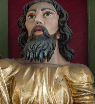 Zdjęcie nr 38: Ołtarz przyścienny, architektoniczny, trójosiowy, dwukondygnacyjny ze zwieńczeniem. Nastawa umieszczona na wysokim, dwudzielnym cokole w górnej części zdobionym na przemian dekoracją płycinową i motywem muszli palmetowej z podwieszoną girlandą kwiatową oraz rozetkami. Cokół wieńczy profilowany gzyms dekorowany kostkowaniem. Antepedium współczesne, marmurowe z umieszczonym centralnie prostym, równoramiennym krzyżem. Na mensie ustawione tabernakulum z tronem wystawienia, o formach architektonicznych, ujęte zdwojonymi, smukłymi kolumienkami o złoconych trzonach umieszczonymi na wysokich cokołach. Podpory dźwigają odcinki pełnego belkowania, na których ustawione złocone figury klęczących aniołów. Część centralna o linii wypukłej, dwukondygnacyjna. W kondygnacji pierwszej złocone drzwiczki z płaskorzeźbionym kielichem z hostią na tle glorii promienistej, powyżej, w kondygnacji drugiej tron wystawienia ujęty rzeźbioną, złoconą kotarą. W zwieńczeniu srebrzona figura baranka apokaliptycznego leżącego na księdze. Nastawa ujęta zdwojonymi, kompozytowymi kolumnami o złoconych trzonach i kapitelach. Pomiędzy kolumnami, w niszach rzeźbione figury św. Piotra (z lewej) i św. Pawła (z prawej), ponad którymi motyw symetrycznie podwieszonej kotary. Kolumny dźwigają odcinki pełnego belkowania z fryzem dekorowanym rozetkami i uskrzydlonymi główkami anielskimi oraz wydatnym gzymsem dekorowanym kostkowaniem. Na osi wewnętrznej pary komun dodatkowo ustawione odcinki półkolistego tympanonu, na których siedzą putta. W polu głównym ołtarza złocona, profilowana rama w kształcie stojącego prostokąta zamkniętego łukiem nadwieszonym mieszcząca barokowy obraz Matki Boskiej z Dzieciątkiem. Nieco powyżej, w osi ołtarza dwa putta unoszące złoconą koronę typu zamkniętego zwieńczoną krzyżem. Kondygnacja druga ujęta parą pilastrów o kompozytowych kapitelach oraz uszami w formie spływów wolutowych, na których siedzące putta. W polu złocona i profilowana rama w kształcie stojącego prostokąta mieszcząca obraz przedstawiający Trójcę Świętą. Całość ołtarza wieńczy profilowany gzyms dekorowany kostkowaniem i zamknięty niskim, trójkątnym przyczółkiem. W polu tympanonu uskrzydlona główka anielska. Struktura ołtarza polichromowana w kolorze jasnozielonym z elementami czerwieni i bieli. Detale architektoniczne, ornamenty oraz szaty postaci złocone.

