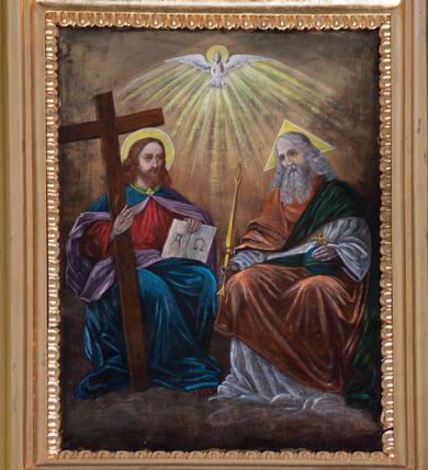 Zdjęcie nr 1: Obraz w kształcie stojącego prostokąta w złoconej, profilowanej ramie dekorowanej motywem kimationu. W centrum kompozycji przedstawiona Trójca Święta – Bóg Ojciec, Chrystus oraz Duch Święty ukazani na tle obłoków. Z prawej strony kompozycji siedzący Bóg Ojciec zwrócony w trzech czwartych w prawo. Postać została ukazana jako starszy mężczyzna z długimi, siwymi i lekko falowanymi włosami oraz taką samą brodą. Pochyla głowę w kierunku siedzącego po jego prawej stronie Chrystusa. W prawym ręku trzyma złote berło zwieńczone krzyżem, lewą wspiera na globie również zamkniętym od góry złotym krzyżem. Bóg Ojciec ubrany jest w obszerne szaty: białą tunikę z długimi rękawami oraz zielono-pomarańczowy płaszcz luźno udrapowany na ramionach. Wokół głowy postaci umieszczony jest trójkątny nimb w kolorze żółtym. Ukazany z lewej strony obrazu Chrystus siedzi, zwracając się w trzech czwartych w lewo. Został przedstawiony jako młody mężczyzna o długich, brązowych włosach i krótkiej brodzie. Jego wzrok skierowany jest ku górze. W prawej ręce z widocznymi śladami męki trzyma krzyż, lewą wspiera na otwartej księdze z literami „A” i „Ω”. Postać ubrana jest w czerwoną tunikę z długimi rękawami oraz spięty pod szyją ciemnoniebieski płaszcz z fioletową podszewką. Wokół szyi dodatkowo złota lamówka. Spod szat widoczne są bose stopy postaci. Wokół głowy Chrystusa umieszczony nimb malowany kolorem żółtym. W górnej części obrazu, w osi kompozycji, przedstawiona gołębica Ducha Świętego na tle promieni. Wokół głowy gołębicy nimb. Tło malowane w odcieniach brązu.
