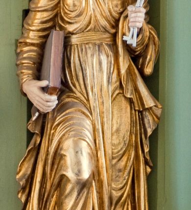 Zdjęcie nr 1: Rzeźba drążona ustawiona na niewielkim, prostopadłościennym postumencie. Święty Piotr został przedstawiony całopostaciowo, w pozycji stojącej z prawą nogą wspartą na kamieniu. W lewej ręce trzyma dwa srebrne klucze, na prawej, opuszczonej wzdłuż tułowia podtrzymuje księgę. Święty został przedstawiony jako starszy mężczyzna o wyrazistych rysach twarzy – głęboko osadzonych oczach, krótkim i wąskim nosie oraz wystających kościach policzkowych. Na głowie siwe, kręcone włosy przerzedzone ponad czołem oraz również siwy zarost. Wzrok postaci skierowany ku górze. Święty Piotr jest ubrany w złocone, bogato fałdowane szaty – sięgającą ziemi suknię z długimi, wąskimi rękawami przewiązaną w pasie oraz złoty płaszcz udrapowany wokół lewej ręki. Widoczne spod szat stopy postaci są bose. Figura polichromowana, partie szat złocone.

