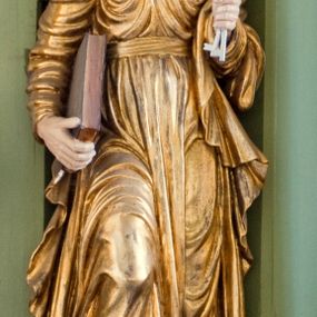 Zdjęcie nr 1: Rzeźba drążona ustawiona na niewielkim, prostopadłościennym postumencie. Święty Piotr został przedstawiony całopostaciowo, w pozycji stojącej z prawą nogą wspartą na kamieniu. W lewej ręce trzyma dwa srebrne klucze, na prawej, opuszczonej wzdłuż tułowia podtrzymuje księgę. Święty został przedstawiony jako starszy mężczyzna o wyrazistych rysach twarzy – głęboko osadzonych oczach, krótkim i wąskim nosie oraz wystających kościach policzkowych. Na głowie siwe, kręcone włosy przerzedzone ponad czołem oraz również siwy zarost. Wzrok postaci skierowany ku górze. Święty Piotr jest ubrany w złocone, bogato fałdowane szaty – sięgającą ziemi suknię z długimi, wąskimi rękawami przewiązaną w pasie oraz złoty płaszcz udrapowany wokół lewej ręki. Widoczne spod szat stopy postaci są bose. Figura polichromowana, partie szat złocone.

