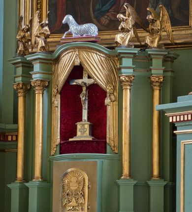 Zdjęcie nr 2: Tabernakulum z tronem wystawienia, jednokondycyjne o formach architektonicznych i wklęsło-wypukłym licu. Ujęte ustawionymi ukośnie, zdwojonymi, złoconymi kolumienkami wspartymi na wysokich cokołach. Kapitele kolumn kompozytowe, dźwigają odcinki pełnego belkowania wyłamanego w osiach podpór. Powyżej pełnoplastyczne, złocone figury klęczących aniołów. Drzwiczki tabernakulum złocone w kształcie stojącego prostokąta zamkniętego łukiem pełnym. Na licu płaskorzeźbiony kielich z hostią na tle glorii promienistej oraz kłosów zboża i winnych gron. Tron wystawienia o linii wypukłej z niszą ujętą płaskorzeźbioną, złoconą kotarą dekorowaną chwostami oraz muszlami palmetowymi. Tło wyłożone aksamitną, czerwoną tkaniną. W zwieńczeniu srebrzony Baranek Eucharystyczny spoczywający na księdze. Struktura tabernakulum malowana w odcieniu seledynowej zieleni, ornamentyka i załamania profili architektonicznych złocone.

