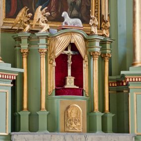 Zdjęcie nr 1: Tabernakulum z tronem wystawienia, jednokondycyjne o formach architektonicznych i wklęsło-wypukłym licu. Ujęte ustawionymi ukośnie, zdwojonymi, złoconymi kolumienkami wspartymi na wysokich cokołach. Kapitele kolumn kompozytowe, dźwigają odcinki pełnego belkowania wyłamanego w osiach podpór. Powyżej pełnoplastyczne, złocone figury klęczących aniołów. Drzwiczki tabernakulum złocone w kształcie stojącego prostokąta zamkniętego łukiem pełnym. Na licu płaskorzeźbiony kielich z hostią na tle glorii promienistej oraz kłosów zboża i winnych gron. Tron wystawienia o linii wypukłej z niszą ujętą płaskorzeźbioną, złoconą kotarą dekorowaną chwostami oraz muszlami palmetowymi. Tło wyłożone aksamitną, czerwoną tkaniną. W zwieńczeniu srebrzony Baranek Eucharystyczny spoczywający na księdze. Struktura tabernakulum malowana w odcieniu seledynowej zieleni, ornamentyka i załamania profili architektonicznych złocone.

