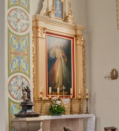 Zdjęcie nr 2: Ołtarz o formach architektonicznych, jednokondygnacyjny ze zwieńczeniem i akantowymi uszami wzbogaconymi o motywy kwiatowe. Mensa kamienna w formie stołu wspartego na dwóch filarach, umieszczona na dwustopniowym podwyższeniu. Na mensie prostopadłościenne tabernakulum ujęte złoconymi kolumienkami oraz zwieńczone złoconym, profilowanym gzymsem. Na drzwiczkach prostokątna płycina zwieńczona łukiem wklęsło-wypukłym. Nastawa drewniana ustawiona na cokole o dekoracji płycinowej, ujęta kanelowanymi pilastrami z kompozytowymi kapitelami z motywem podwieszonej kampanuli. W prostokątnym polu ołtarza obraz „Jezu Ufam Tobie” w złoconej i profilowanej ramie. Podpory dźwigają niepełne belkowanie z wydatnym gzymsem wyłamanym na osi pilastrów. Zwieńczenie prostokątne zamknięte profilowanym gzymsem o lini wklęsło-wypukłej, ujęte po bokach spływami wolutowymi. W polu zwieńczenia obraz w kształcie stojącego prostokąta zamkniętego łukiem wyniesionym mieszczący wizerunek św. Barbary. Całość ołtarza zwieńczona glorią promienistą z Okiem Opatrzności na czerwonym tle, ujętym medalionem utworzonym ze srebrzonych obłoków. Struktura ołtarza malowana w odcieniach beżu, detal ramy obrazu w polu głównym nastawy w kolorze czerwonym. Ornamentyka oraz załamania profili architektonicznych złocone.
