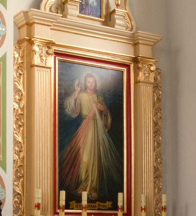 Zdjęcie nr 1: Ołtarz o formach architektonicznych, jednokondygnacyjny ze zwieńczeniem i akantowymi uszami wzbogaconymi o motywy kwiatowe. Mensa kamienna w formie stołu wspartego na dwóch filarach, umieszczona na dwustopniowym podwyższeniu. Na mensie prostopadłościenne tabernakulum ujęte złoconymi kolumienkami oraz zwieńczone złoconym, profilowanym gzymsem. Na drzwiczkach prostokątna płycina zwieńczona łukiem wklęsło-wypukłym. Nastawa drewniana ustawiona na cokole o dekoracji płycinowej, ujęta kanelowanymi pilastrami z kompozytowymi kapitelami z motywem podwieszonej kampanuli. W prostokątnym polu ołtarza obraz „Jezu Ufam Tobie” w złoconej i profilowanej ramie. Podpory dźwigają niepełne belkowanie z wydatnym gzymsem wyłamanym na osi pilastrów. Zwieńczenie prostokątne zamknięte profilowanym gzymsem o lini wklęsło-wypukłej, ujęte po bokach spływami wolutowymi. W polu zwieńczenia obraz w kształcie stojącego prostokąta zamkniętego łukiem wyniesionym mieszczący wizerunek św. Barbary. Całość ołtarza zwieńczona glorią promienistą z Okiem Opatrzności na czerwonym tle, ujętym medalionem utworzonym ze srebrzonych obłoków. Struktura ołtarza malowana w odcieniach beżu, detal ramy obrazu w polu głównym nastawy w kolorze czerwonym. Ornamentyka oraz załamania profili architektonicznych złocone.
