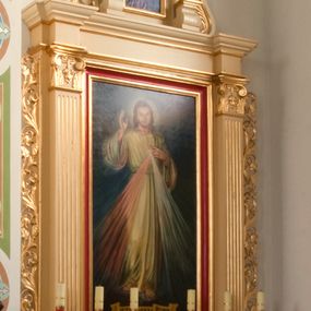 Zdjęcie nr 1: Ołtarz o formach architektonicznych, jednokondygnacyjny ze zwieńczeniem i akantowymi uszami wzbogaconymi o motywy kwiatowe. Mensa kamienna w formie stołu wspartego na dwóch filarach, umieszczona na dwustopniowym podwyższeniu. Na mensie prostopadłościenne tabernakulum ujęte złoconymi kolumienkami oraz zwieńczone złoconym, profilowanym gzymsem. Na drzwiczkach prostokątna płycina zwieńczona łukiem wklęsło-wypukłym. Nastawa drewniana ustawiona na cokole o dekoracji płycinowej, ujęta kanelowanymi pilastrami z kompozytowymi kapitelami z motywem podwieszonej kampanuli. W prostokątnym polu ołtarza obraz „Jezu Ufam Tobie” w złoconej i profilowanej ramie. Podpory dźwigają niepełne belkowanie z wydatnym gzymsem wyłamanym na osi pilastrów. Zwieńczenie prostokątne zamknięte profilowanym gzymsem o lini wklęsło-wypukłej, ujęte po bokach spływami wolutowymi. W polu zwieńczenia obraz w kształcie stojącego prostokąta zamkniętego łukiem wyniesionym mieszczący wizerunek św. Barbary. Całość ołtarza zwieńczona glorią promienistą z Okiem Opatrzności na czerwonym tle, ujętym medalionem utworzonym ze srebrzonych obłoków. Struktura ołtarza malowana w odcieniach beżu, detal ramy obrazu w polu głównym nastawy w kolorze czerwonym. Ornamentyka oraz załamania profili architektonicznych złocone.
