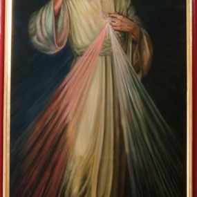 Zdjęcie nr 1: Obraz w kształcie stojącego prostokąta ujęty profilowaną i częściowo złoconą ramą. W centrum kompozycji postać Chrystusa zwróconego frontalnie, który lewą ręką dotyka rany na piersi, prawą unosi w geście błogosławieństwa. Postać ubrana jest w białą szatę o szerokich rękawach, przepasaną w talii. Z boku wydobywają się dwie wiązki promieni czerwona i niebieska. Wokół głowy widoczny świetlisty nimb. Jezus stoi na obłokach. Tło obrazu jednolicie ciemnoszare. U dołu obrazu banderola z napisem „JEZU UFAM TOBIE”. 