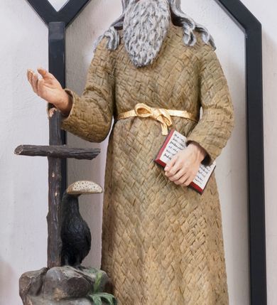 Zdjęcie nr 1: Rzeźba pełnoplastyczna umieszczona na niewielkim, prostopadłościennym postumencie, na którym ustawiona jest także skała zwieńczona drewnianym krzyżem oraz kruk z chlebem w dziobie. Święty Benedykt ukazany w pozycji stojącej, frontalnie. Został przedstawiony jako starszy mężczyzna o długich, siwych włosach oraz długiej, kędzierzawej brodzie w tym samym kolorze ubrany w długą, pustelniczą szatę przepasaną złotym sznurem. Głowa uniesiona ku górze, oczy szeroko otwarte. W lewej ręce święty trzyma otwartą księgę, prawą wyciąga przed siebie. Rzeźba w pełni polichromowana, pas złocony.