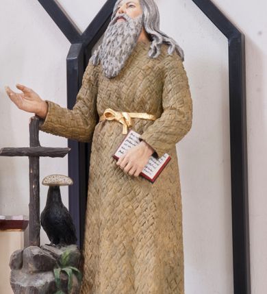 Zdjęcie nr 2: Rzeźba pełnoplastyczna umieszczona na niewielkim, prostopadłościennym postumencie, na którym ustawiona jest także skała zwieńczona drewnianym krzyżem oraz kruk z chlebem w dziobie. Święty Benedykt ukazany w pozycji stojącej, frontalnie. Został przedstawiony jako starszy mężczyzna o długich, siwych włosach oraz długiej, kędzierzawej brodzie w tym samym kolorze ubrany w długą, pustelniczą szatę przepasaną złotym sznurem. Głowa uniesiona ku górze, oczy szeroko otwarte. W lewej ręce święty trzyma otwartą księgę, prawą wyciąga przed siebie. Rzeźba w pełni polichromowana, pas złocony.