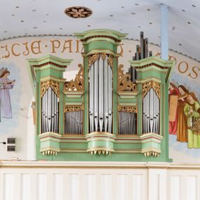 Zdjęcie nr 1: Prospekt organowy jednokondygnacyjny, pięcioosiowy o formach architektonicznych umieszczony na wysokim cokole.
Osie nieparzyste (pierwsza, trzecia i piąta) z większymi piszczałkami wypukłe, a pierwsza i piąta, na rzucie trójkąta niższe od środkowej. Wszystkie zwieńczone pełnym belkowaniem z wydatnym, profilowanym gzymsem dekorowanym kostkowaniem. W górnej części złocony, ażurowy lambrekin utworzony z ornamentu małżowinowo-chrząstkowego. Osie parzyste są niższe z płaskimi, prostokątnymi niszami mieszczącymi mniejsze piszczałki. Wieńczą je profilowano-fazowane konsole oraz ażurowe struktury z ornamentu małżowinowo-chrząstkowego. Prospekt polichromowany w odcieniach seledynowej zieleni z czerwonymi detalami, zaś ornamentyka i załamania profili architektonicznych złocone.