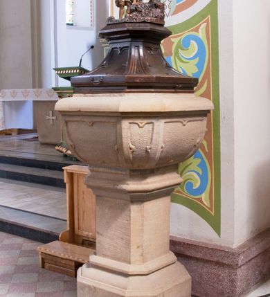 Zdjęcie nr 1: Chrzcielnica ustawiona na prostopadłościennej podstawie.  Profilowany cokół o przekroju prostokąta o ściętych narożach, trzon o takim samym przekroju ujęty u góry i u dołu profilowanymi wałkami. Czara spłaszczona o przekroju czworoboku o ściętych narożach; z wylewem. Pola z płycinową dekoracją peudomaswerkową. Pokrywa drewniana o dekoracji analogicznej jak czara, zwieńczona pełnoplastyczną, rzeźbioną sceną Chrztu Chrystusa.
