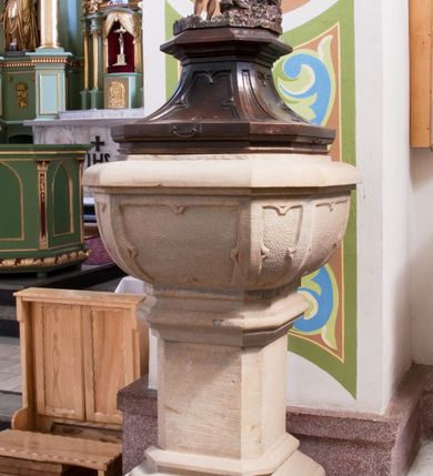 Zdjęcie nr 2: Chrzcielnica ustawiona na prostopadłościennej podstawie.  Profilowany cokół o przekroju prostokąta o ściętych narożach, trzon o takim samym przekroju ujęty u góry i u dołu profilowanymi wałkami. Czara spłaszczona o przekroju czworoboku o ściętych narożach; z wylewem. Pola z płycinową dekoracją peudomaswerkową. Pokrywa drewniana o dekoracji analogicznej jak czara, zwieńczona pełnoplastyczną, rzeźbioną sceną Chrztu Chrystusa.
