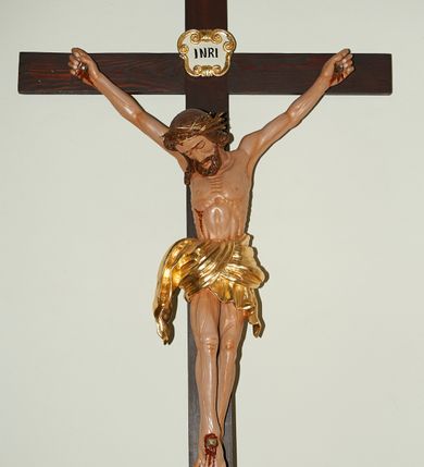 Zdjęcie nr 1: Wizerunek Chrystusa przybitego trzema gwoździami do krzyża.  Ciało wyprostowane, o wyraźnie wyeksponowanej linii żeber i muskulaturze, długie i szczupłe ręce rozciągnięte powyżej głowy, nogi delikatnie ugięte w kolanach, prawe kolano powyżej lewego. Głowa pochylona na prawy bark. Twarz szczupła, oczy zamknięte, nos prosty. Włosy długie, ciemnobrązowe, lekko falowane opadające na prawe ramię postaci. Na twarzy ciemny zarost – krótka, ciemnobrązowa broda i wąsy. Na głowie złocona korona cierniowa. Biodra otacza krótkie, złote perizonium przewiązane w węzeł. W miejscach przebić gwoździami oraz na ranie w boku ślady krwi. Krzyż gładki, ciemnobrązowy, na górnej belce titulus w formie złoconego, wolutowego kartusza z napisem  „INRI” (łac. Iesus Nazarenus Rex Iudaeorum) na białym tle. Figura w pełni polichromowana, partie szat złocone.
