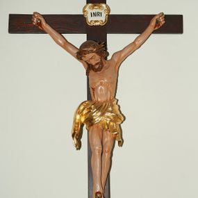 Zdjęcie nr 1: Wizerunek Chrystusa przybitego trzema gwoździami do krzyża.  Ciało wyprostowane, o wyraźnie wyeksponowanej linii żeber i muskulaturze, długie i szczupłe ręce rozciągnięte powyżej głowy, nogi delikatnie ugięte w kolanach, prawe kolano powyżej lewego. Głowa pochylona na prawy bark. Twarz szczupła, oczy zamknięte, nos prosty. Włosy długie, ciemnobrązowe, lekko falowane opadające na prawe ramię postaci. Na twarzy ciemny zarost – krótka, ciemnobrązowa broda i wąsy. Na głowie złocona korona cierniowa. Biodra otacza krótkie, złote perizonium przewiązane w węzeł. W miejscach przebić gwoździami oraz na ranie w boku ślady krwi. Krzyż gładki, ciemnobrązowy, na górnej belce titulus w formie złoconego, wolutowego kartusza z napisem  „INRI” (łac. Iesus Nazarenus Rex Iudaeorum) na białym tle. Figura w pełni polichromowana, partie szat złocone.