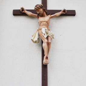 Zdjęcie nr 1: Pełnoplastyczna i w pełni polichromowana figura Ukrzyżowanego Chrystusa. Ciało Zbawiciela o nienaturalnych proporcjach z dużą głową oraz krótkimi ramionami. Chrystus został przedstawiony jako mężczyzna o długich, brązowych włosach opadających na ramiona w spiralnie skręconych lokach. Głowa postaci pochylona na prawe ramię. Oczy zamknięte, długi, prosty nos. Na głowie złocona korona cierniowa. Stopy przebite jednym gwoździem. Z dłoni, stóp oraz rany w boku płynie krew. Perizonium białe, krótkie luźno udrapowane wokół podwójnego, złoconego sznura zakończonego chwostami opadającymi wzdłuż prawego uda postaci.