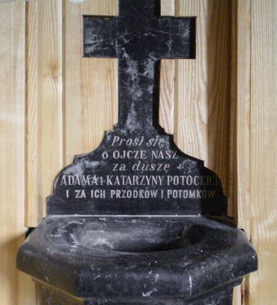 Zdjęcie nr 1: Kropielnica wmurowana w ścianę, na rzucie pięcioboku, z wewnętrznym półkulistym pojemnikiem na wodę, o bocznych ściankach z ślepymi zakończonymi półkoliście arkadkami. Nad kropielnicą krzyż na szerokiej podstawie o wykroju wklęsło-wypukłym z inskrypcją „Prosi się / o OJCZE NASZ / za duszę / ADAMA I KATARZYNY POTOCKICH / ZA ICH PRZODKÓW I POTOMKÓW”. Od dołu widoczna podtrzymująca czarę profilowana konsola zakończona kulistą gałką. 