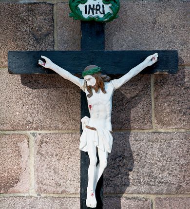 Zdjęcie nr 1: Pełnoplastyczna, polichromowana figura Chrystusa na krzyżu. Sylwetka zmarłego jest smukła, o białej karnacji,  z wyraźnie zaznaczoną muskulaturą i układem kostnym. Ramiona rozpostarte, uniesione powyżej głowy, nogi są lekko ugięte w kolanach, przechylone na prawą stronę. Głowa opada na prawe ramię, twarz pociągła, oczy otwarte, nos o prostym profilu, usta rozchylone. Włosy ciemne, spływają na plecy i ramiona, twarz okala krótka broda. Na głowie ciemnozielona korona cierniowa, biodra otoczone białym, krótkim perizonium podtrzymywanym brązowym sznurem, opadające pionowymi fałdami z przodu i na prawy bok. Na ciele Chrystusa widoczne są ślady męki: przebity bok, dłonie oraz stopy. Nad głową titulus z napisem „INRI” ujęty liśćmi; krzyż czarny. 