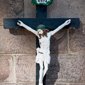 Zdjęcie nr 1: Pełnoplastyczna, polichromowana figura Chrystusa na krzyżu. Sylwetka zmarłego jest smukła, o białej karnacji,  z wyraźnie zaznaczoną muskulaturą i układem kostnym. Ramiona rozpostarte, uniesione powyżej głowy, nogi są lekko ugięte w kolanach, przechylone na prawą stronę. Głowa opada na prawe ramię, twarz pociągła, oczy otwarte, nos o prostym profilu, usta rozchylone. Włosy ciemne, spływają na plecy i ramiona, twarz okala krótka broda. Na głowie ciemnozielona korona cierniowa, biodra otoczone białym, krótkim perizonium podtrzymywanym brązowym sznurem, opadające pionowymi fałdami z przodu i na prawy bok. Na ciele Chrystusa widoczne są ślady męki: przebity bok, dłonie oraz stopy. Nad głową titulus z napisem „INRI” ujęty liśćmi; krzyż czarny. 