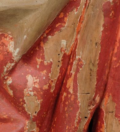 Zdjęcie nr 4: Rzeźba pełnoplastyczna, z tyłu opracowana, drążona wewnątrz, ustawiona na wielobocznej podstawie. Chrystus ukazany frontalnie, w pozycji stojącej, w lekkim kontrapoście, z prawą stopą wysuniętą do przodu, korpus przechylony w lewą stronę, prawy bark podniesiony wyżej od lewego. Prawa ręka wzniesiona ku górze w geście błogosławieństwa, lewa mocno przylega do ciała w okolicy żeber, ugięta w łokciu, w której trzyma drzewce proporca. Twarz pociągła o karnacji cielistej, z zaróżowionymi policzkami, wysokie czoło, szeroko rozstawione, podłużne oczy ze źrenicami i zarysowaną powieką, zaznaczone brwi cienką kreską, długi, prosty nos, wąskie usta. Okala ją zarost oraz długie, gładkie, delikatnie sfalowane włosy, z przedziałkiem, zasłaniające uszy i opadające na kark oraz plecy. W prawym boku i na stopach wyraźne rany. Odziany jest w szatę upiętą pod szyją, w czerwonym kolorze z ciemno- granatową podszewką i złotą lamówką, odsłaniającą tors i wklęsły brzuch, z prawą połą przerzuconą z przodu pod prawą ręką i zawiniętą wokół lewego przedramienia. Fałdy płaszcza są załamane ostro, diagonalnie i nieckowato. Na boku, stopie i lewej ręce zaznaczone rany.