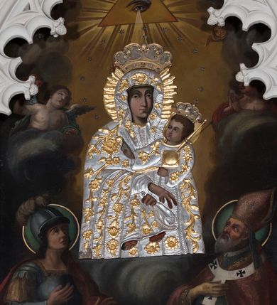 Zdjęcie nr 3: Obraz o kształcie stojącego prostokąta zamkniętego łukiem ostrym. Pośrodku, wśród obłoków przedstawienie Matki Boskiej z Dzieciątkiem na lewym ramieniu, w półpostaci, zwrócona lekko w lewo, z dłońmi skrzyżowanymi w okolicach kolan Chrystusa. Po bokach adorujący dwaj aniołowie Poniżej w narożach kompozycji klęczą po stronie lewej św. Jerzy, po prawej św. Wojciech. Ponad Marią Oko Opatrzności. Matka Boska ubrana jest w czerwoną suknię ze złotą lamówką, na która narzucony ma błękitny płaszcz z kwiatami o żółtych środkach. Głowę wieńczy dekoracyjna korona, podobnie jak Jezusa. Chrystus ukazany jest en trois quarts, w swobodnej pozycji, lewą ręką podtrzymuje  księgę włożoną pod pachę, prawą unosi w geście błogosławieństwa. Ubrany jest w długą sukienkę z długimi rękawami, przewiązaną paskiem, odsłaniającą stopy.  Św. Jerzy, w zbroi i czerwonym płaszczu narzuconym na ramiona, prawą rękę przyłożył do klatki piersiowej, lewą unosi w okolicy tułowia. Na głowie ma hełm z pióropuszem, spod którego widać długie, kręcone włosy opadające na kark. Przy lewym jego boku widoczna jest głowa zabitego smoka. Św. Wojciech, w stroju pontyfikalnym, z paliuszem na ramionach, prawą rękę położył na klatce piersiowej, lewą podtrzymuje połę kapy liturgicznej. Wokół głów świętych koliste nimby. 