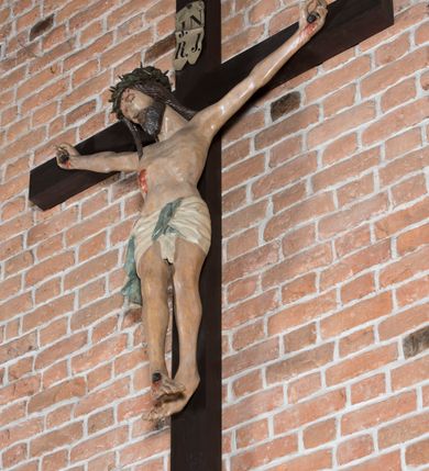 Zdjęcie nr 3: Rzeźba pełnoplastyczna, polichromowana. Chrystus w niezbyt głębokim zwisie o sztywnych, mocno napiętych, rozpostartych ramionach i delikatnie zwiniętych palcach. Nogi wyprostowane, skierowane do wewnątrz, dosyć duże stopy nałożone prawa na lewą i przybite jednym gwoździem. Na biodrach krótkie perizonium, z przewagą fałd pionowych, opada na prawym boku kaskadą, z kolei drugi koniec wywinięty na perizonium i spływa na lewe udo. Głowa lekko pochylona w kierunku prawego ramienia, oczy zamknięte, brwi opadające w kierunku skroni, nos prosty, długi, twarz pociągła o wyraźnych kościach policzkowych, usta wąskie, lekko uchylone, okolone przez schematycznie opracowaną w symetryczne rowki brodę. Na głowie korona cierniowa w formie dwóch wałków z licznymi kolcami, spod której opada na prawe ramię cienkie pasmo schematycznie rytych włosów. Z miejsc po przebiciu gwoździami, z rany zadanej w boku oraz spod korony cierniowej spływa krew. Karnacja Chrystusa dosyć jasna, z odcieniem szarości. Krzyż, zarost, włosy, korona cierniowa w kolorze ciemnobrązowym, perizonium białe. W górnej części pionowej belki krzyża zawieszona w pionie tabliczka, dosyć długa, o zwiniętych do wewnątrz końcach, z trójkątnymi wycięciami na środku brzegów, z napisem „I.N.R.I”.