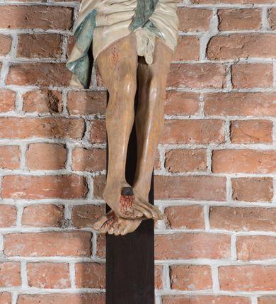 Zdjęcie nr 8: Rzeźba pełnoplastyczna, polichromowana. Chrystus w niezbyt głębokim zwisie o sztywnych, mocno napiętych, rozpostartych ramionach i delikatnie zwiniętych palcach. Nogi wyprostowane, skierowane do wewnątrz, dosyć duże stopy nałożone prawa na lewą i przybite jednym gwoździem. Na biodrach krótkie perizonium, z przewagą fałd pionowych, opada na prawym boku kaskadą, z kolei drugi koniec wywinięty na perizonium i spływa na lewe udo. Głowa lekko pochylona w kierunku prawego ramienia, oczy zamknięte, brwi opadające w kierunku skroni, nos prosty, długi, twarz pociągła o wyraźnych kościach policzkowych, usta wąskie, lekko uchylone, okolone przez schematycznie opracowaną w symetryczne rowki brodę. Na głowie korona cierniowa w formie dwóch wałków z licznymi kolcami, spod której opada na prawe ramię cienkie pasmo schematycznie rytych włosów. Z miejsc po przebiciu gwoździami, z rany zadanej w boku oraz spod korony cierniowej spływa krew. Karnacja Chrystusa dosyć jasna, z odcieniem szarości. Krzyż, zarost, włosy, korona cierniowa w kolorze ciemnobrązowym, perizonium białe. W górnej części pionowej belki krzyża zawieszona w pionie tabliczka, dosyć długa, o zwiniętych do wewnątrz końcach, z trójkątnymi wycięciami na środku brzegów, z napisem „I.N.R.I”.