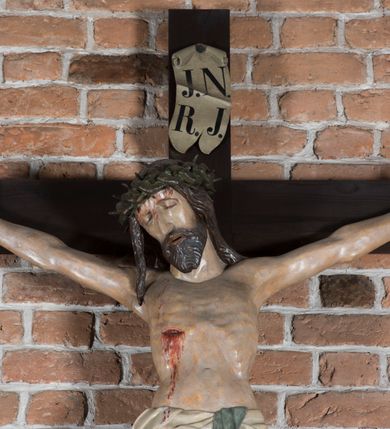 Zdjęcie nr 7: Rzeźba pełnoplastyczna, polichromowana. Chrystus w niezbyt głębokim zwisie o sztywnych, mocno napiętych, rozpostartych ramionach i delikatnie zwiniętych palcach. Nogi wyprostowane, skierowane do wewnątrz, dosyć duże stopy nałożone prawa na lewą i przybite jednym gwoździem. Na biodrach krótkie perizonium, z przewagą fałd pionowych, opada na prawym boku kaskadą, z kolei drugi koniec wywinięty na perizonium i spływa na lewe udo. Głowa lekko pochylona w kierunku prawego ramienia, oczy zamknięte, brwi opadające w kierunku skroni, nos prosty, długi, twarz pociągła o wyraźnych kościach policzkowych, usta wąskie, lekko uchylone, okolone przez schematycznie opracowaną w symetryczne rowki brodę. Na głowie korona cierniowa w formie dwóch wałków z licznymi kolcami, spod której opada na prawe ramię cienkie pasmo schematycznie rytych włosów. Z miejsc po przebiciu gwoździami, z rany zadanej w boku oraz spod korony cierniowej spływa krew. Karnacja Chrystusa dosyć jasna, z odcieniem szarości. Krzyż, zarost, włosy, korona cierniowa w kolorze ciemnobrązowym, perizonium białe. W górnej części pionowej belki krzyża zawieszona w pionie tabliczka, dosyć długa, o zwiniętych do wewnątrz końcach, z trójkątnymi wycięciami na środku brzegów, z napisem „I.N.R.I”.