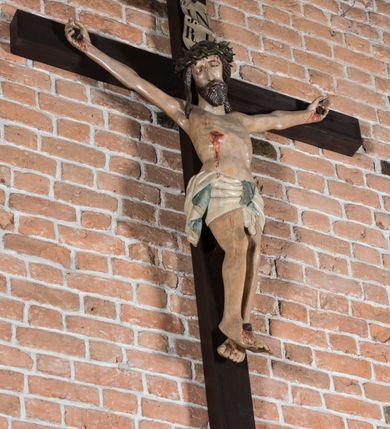 Zdjęcie nr 4: Rzeźba pełnoplastyczna, polichromowana. Chrystus w niezbyt głębokim zwisie o sztywnych, mocno napiętych, rozpostartych ramionach i delikatnie zwiniętych palcach. Nogi wyprostowane, skierowane do wewnątrz, dosyć duże stopy nałożone prawa na lewą i przybite jednym gwoździem. Na biodrach krótkie perizonium, z przewagą fałd pionowych, opada na prawym boku kaskadą, z kolei drugi koniec wywinięty na perizonium i spływa na lewe udo. Głowa lekko pochylona w kierunku prawego ramienia, oczy zamknięte, brwi opadające w kierunku skroni, nos prosty, długi, twarz pociągła o wyraźnych kościach policzkowych, usta wąskie, lekko uchylone, okolone przez schematycznie opracowaną w symetryczne rowki brodę. Na głowie korona cierniowa w formie dwóch wałków z licznymi kolcami, spod której opada na prawe ramię cienkie pasmo schematycznie rytych włosów. Z miejsc po przebiciu gwoździami, z rany zadanej w boku oraz spod korony cierniowej spływa krew. Karnacja Chrystusa dosyć jasna, z odcieniem szarości. Krzyż, zarost, włosy, korona cierniowa w kolorze ciemnobrązowym, perizonium białe. W górnej części pionowej belki krzyża zawieszona w pionie tabliczka, dosyć długa, o zwiniętych do wewnątrz końcach, z trójkątnymi wycięciami na środku brzegów, z napisem „I.N.R.I”.