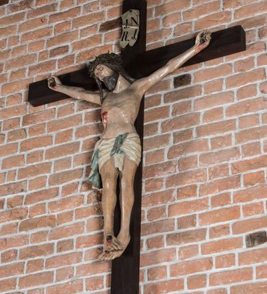 Zdjęcie nr 9: Rzeźba pełnoplastyczna, polichromowana. Chrystus w niezbyt głębokim zwisie o sztywnych, mocno napiętych, rozpostartych ramionach i delikatnie zwiniętych palcach. Nogi wyprostowane, skierowane do wewnątrz, dosyć duże stopy nałożone prawa na lewą i przybite jednym gwoździem. Na biodrach krótkie perizonium, z przewagą fałd pionowych, opada na prawym boku kaskadą, z kolei drugi koniec wywinięty na perizonium i spływa na lewe udo. Głowa lekko pochylona w kierunku prawego ramienia, oczy zamknięte, brwi opadające w kierunku skroni, nos prosty, długi, twarz pociągła o wyraźnych kościach policzkowych, usta wąskie, lekko uchylone, okolone przez schematycznie opracowaną w symetryczne rowki brodę. Na głowie korona cierniowa w formie dwóch wałków z licznymi kolcami, spod której opada na prawe ramię cienkie pasmo schematycznie rytych włosów. Z miejsc po przebiciu gwoździami, z rany zadanej w boku oraz spod korony cierniowej spływa krew. Karnacja Chrystusa dosyć jasna, z odcieniem szarości. Krzyż, zarost, włosy, korona cierniowa w kolorze ciemnobrązowym, perizonium białe. W górnej części pionowej belki krzyża zawieszona w pionie tabliczka, dosyć długa, o zwiniętych do wewnątrz końcach, z trójkątnymi wycięciami na środku brzegów, z napisem „I.N.R.I”.