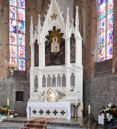 Zdjęcie nr 7: Neogotycki ołtarz główny w kolorze naturalnego wapienia, architektoniczny, wolnostojący, trójosiowy, z wydzieloną częścią cokołową, dwukondygnacyjny, ze zwieńczeniem. Mensa skrzyniowa, ujęta dwiema kolumienkami. Antependium ozdobione płycinami w kształcie czworoliści. Nastawa artykułowana w dolnej kondygnacji czworobocznymi półfilarami, w górnej kondygnacji kolumienkami o liściastych kapitelach, z opaskami w połowie wysokości, przechodzącymi w zwieńczeniu w pinakle. Dolna kondygnacja dwustrefowa. W strefie dolnej stylizowana wić roślinna i tarcze herbowe. W strefie górnej nisze zamknięte trójlistnie (na relikwiarze?), w osi środkowej pięć, w osiach skrajnych po jednej. W kondygnacji górnej nisze, środkowa szeroka, zamknięta ostrołukowo z maswerkowaniem w podłuczu, w osiach skrajnych wąskie, zamknięte trójlistnie. W niszy środkowej obraz Adoracja Matki Boskiej Śnieżnej przez śś. Wojciecha i Jerzego, po bokach obrazy: po prawej Św. Florian, z sygnaturą w dolnej części -  S. Bryniarski / pinxit 1886; po lewej postać kobiety w prawej ręce ze zwojem z napisem: EWAN/GELJA, z sygnaturą u dołu - S. Bryniarski / malował. W zwieńczeniu pomiędzy pinaklami trójkątne szczyty z żabkami na krawędziach, środkowy w polu z rozetą z Gołębicą Ducha Świętego na złotym tle, zakończony krzyżem. 