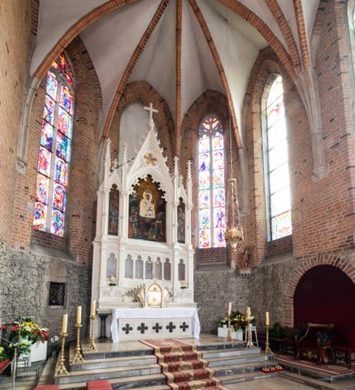 Zdjęcie nr 21: Neogotycki ołtarz główny w kolorze naturalnego wapienia, architektoniczny, wolnostojący, trójosiowy, z wydzieloną częścią cokołową, dwukondygnacyjny, ze zwieńczeniem. Mensa skrzyniowa, ujęta dwiema kolumienkami. Antependium ozdobione płycinami w kształcie czworoliści. Nastawa artykułowana w dolnej kondygnacji czworobocznymi półfilarami, w górnej kondygnacji kolumienkami o liściastych kapitelach, z opaskami w połowie wysokości, przechodzącymi w zwieńczeniu w pinakle. Dolna kondygnacja dwustrefowa. W strefie dolnej stylizowana wić roślinna i tarcze herbowe. W strefie górnej nisze zamknięte trójlistnie (na relikwiarze?), w osi środkowej pięć, w osiach skrajnych po jednej. W kondygnacji górnej nisze, środkowa szeroka, zamknięta ostrołukowo z maswerkowaniem w podłuczu, w osiach skrajnych wąskie, zamknięte trójlistnie. W niszy środkowej obraz Adoracja Matki Boskiej Śnieżnej przez śś. Wojciecha i Jerzego, po bokach obrazy: po prawej Św. Florian, z sygnaturą w dolnej części -  S. Bryniarski / pinxit 1886; po lewej postać kobiety w prawej ręce ze zwojem z napisem: EWAN/GELJA, z sygnaturą u dołu - S. Bryniarski / malował. W zwieńczeniu pomiędzy pinaklami trójkątne szczyty z żabkami na krawędziach, środkowy w polu z rozetą z Gołębicą Ducha Świętego na złotym tle, zakończony krzyżem. 