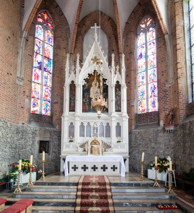 Zdjęcie nr 24: Neogotycki ołtarz główny w kolorze naturalnego wapienia, architektoniczny, wolnostojący, trójosiowy, z wydzieloną częścią cokołową, dwukondygnacyjny, ze zwieńczeniem. Mensa skrzyniowa, ujęta dwiema kolumienkami. Antependium ozdobione płycinami w kształcie czworoliści. Nastawa artykułowana w dolnej kondygnacji czworobocznymi półfilarami, w górnej kondygnacji kolumienkami o liściastych kapitelach, z opaskami w połowie wysokości, przechodzącymi w zwieńczeniu w pinakle. Dolna kondygnacja dwustrefowa. W strefie dolnej stylizowana wić roślinna i tarcze herbowe. W strefie górnej nisze zamknięte trójlistnie (na relikwiarze?), w osi środkowej pięć, w osiach skrajnych po jednej. W kondygnacji górnej nisze, środkowa szeroka, zamknięta ostrołukowo z maswerkowaniem w podłuczu, w osiach skrajnych wąskie, zamknięte trójlistnie. W niszy środkowej obraz Adoracja Matki Boskiej Śnieżnej przez śś. Wojciecha i Jerzego, po bokach obrazy: po prawej Św. Florian, z sygnaturą w dolnej części -  S. Bryniarski / pinxit 1886; po lewej postać kobiety w prawej ręce ze zwojem z napisem: EWAN/GELJA, z sygnaturą u dołu - S. Bryniarski / malował. W zwieńczeniu pomiędzy pinaklami trójkątne szczyty z żabkami na krawędziach, środkowy w polu z rozetą z Gołębicą Ducha Świętego na złotym tle, zakończony krzyżem. 