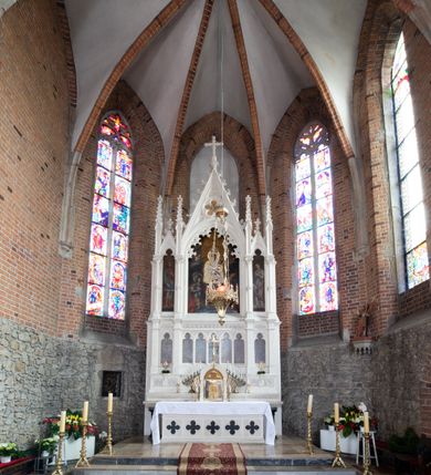 Zdjęcie nr 27: Neogotycki ołtarz główny w kolorze naturalnego wapienia, architektoniczny, wolnostojący, trójosiowy, z wydzieloną częścią cokołową, dwukondygnacyjny, ze zwieńczeniem. Mensa skrzyniowa, ujęta dwiema kolumienkami. Antependium ozdobione płycinami w kształcie czworoliści. Nastawa artykułowana w dolnej kondygnacji czworobocznymi półfilarami, w górnej kondygnacji kolumienkami o liściastych kapitelach, z opaskami w połowie wysokości, przechodzącymi w zwieńczeniu w pinakle. Dolna kondygnacja dwustrefowa. W strefie dolnej stylizowana wić roślinna i tarcze herbowe. W strefie górnej nisze zamknięte trójlistnie (na relikwiarze?), w osi środkowej pięć, w osiach skrajnych po jednej. W kondygnacji górnej nisze, środkowa szeroka, zamknięta ostrołukowo z maswerkowaniem w podłuczu, w osiach skrajnych wąskie, zamknięte trójlistnie. W niszy środkowej obraz Adoracja Matki Boskiej Śnieżnej przez śś. Wojciecha i Jerzego, po bokach obrazy: po prawej Św. Florian, z sygnaturą w dolnej części -  S. Bryniarski / pinxit 1886; po lewej postać kobiety w prawej ręce ze zwojem z napisem: EWAN/GELJA, z sygnaturą u dołu - S. Bryniarski / malował. W zwieńczeniu pomiędzy pinaklami trójkątne szczyty z żabkami na krawędziach, środkowy w polu z rozetą z Gołębicą Ducha Świętego na złotym tle, zakończony krzyżem. 