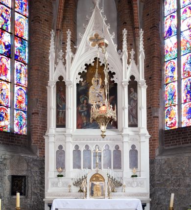 Zdjęcie nr 28: Neogotycki ołtarz główny w kolorze naturalnego wapienia, architektoniczny, wolnostojący, trójosiowy, z wydzieloną częścią cokołową, dwukondygnacyjny, ze zwieńczeniem. Mensa skrzyniowa, ujęta dwiema kolumienkami. Antependium ozdobione płycinami w kształcie czworoliści. Nastawa artykułowana w dolnej kondygnacji czworobocznymi półfilarami, w górnej kondygnacji kolumienkami o liściastych kapitelach, z opaskami w połowie wysokości, przechodzącymi w zwieńczeniu w pinakle. Dolna kondygnacja dwustrefowa. W strefie dolnej stylizowana wić roślinna i tarcze herbowe. W strefie górnej nisze zamknięte trójlistnie (na relikwiarze?), w osi środkowej pięć, w osiach skrajnych po jednej. W kondygnacji górnej nisze, środkowa szeroka, zamknięta ostrołukowo z maswerkowaniem w podłuczu, w osiach skrajnych wąskie, zamknięte trójlistnie. W niszy środkowej obraz Adoracja Matki Boskiej Śnieżnej przez śś. Wojciecha i Jerzego, po bokach obrazy: po prawej Św. Florian, z sygnaturą w dolnej części -  S. Bryniarski / pinxit 1886; po lewej postać kobiety w prawej ręce ze zwojem z napisem: EWAN/GELJA, z sygnaturą u dołu - S. Bryniarski / malował. W zwieńczeniu pomiędzy pinaklami trójkątne szczyty z żabkami na krawędziach, środkowy w polu z rozetą z Gołębicą Ducha Świętego na złotym tle, zakończony krzyżem. 