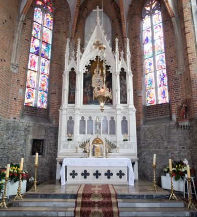 Zdjęcie nr 29: Neogotycki ołtarz główny w kolorze naturalnego wapienia, architektoniczny, wolnostojący, trójosiowy, z wydzieloną częścią cokołową, dwukondygnacyjny, ze zwieńczeniem. Mensa skrzyniowa, ujęta dwiema kolumienkami. Antependium ozdobione płycinami w kształcie czworoliści. Nastawa artykułowana w dolnej kondygnacji czworobocznymi półfilarami, w górnej kondygnacji kolumienkami o liściastych kapitelach, z opaskami w połowie wysokości, przechodzącymi w zwieńczeniu w pinakle. Dolna kondygnacja dwustrefowa. W strefie dolnej stylizowana wić roślinna i tarcze herbowe. W strefie górnej nisze zamknięte trójlistnie (na relikwiarze?), w osi środkowej pięć, w osiach skrajnych po jednej. W kondygnacji górnej nisze, środkowa szeroka, zamknięta ostrołukowo z maswerkowaniem w podłuczu, w osiach skrajnych wąskie, zamknięte trójlistnie. W niszy środkowej obraz Adoracja Matki Boskiej Śnieżnej przez śś. Wojciecha i Jerzego, po bokach obrazy: po prawej Św. Florian, z sygnaturą w dolnej części -  S. Bryniarski / pinxit 1886; po lewej postać kobiety w prawej ręce ze zwojem z napisem: EWAN/GELJA, z sygnaturą u dołu - S. Bryniarski / malował. W zwieńczeniu pomiędzy pinaklami trójkątne szczyty z żabkami na krawędziach, środkowy w polu z rozetą z Gołębicą Ducha Świętego na złotym tle, zakończony krzyżem. 