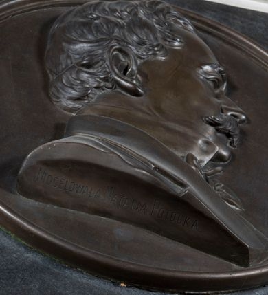 Zdjęcie nr 2: Epitafium w formie kamiennej tablicy, w kształcie stojącego prostokąta, flankowanej po bokach zdwojonymi pilastrami o jońskich kapitelach, posadowionymi na szerokim, profilowanym gzymsie z podwieszonymi ulistnionymi wolutami, dźwigającymi przełamane belkowanie, z wydatnym gzymsem, zwieńczone przyczółkiem w kształcie łuku odcinkowego. Na przyczółku cokolik ujęty wolutkami i krzyż o rozszerzających się ramionach, zaś w polu kartusz z godłem herbu Pilawa. Pośrodku epitafium okrągły medalion z popiersiem zmarłego, ukazanym z prawego profilu, w marynarce z muszką. Jego twarz jest pełna, nos krótki, wydatny, włosy kręcone, a twarz zdobią długie, sumiaste wąsy. W fryzie belkowania inskrypcja „D(EO) O(PTIMO) M(AXIMO)”, a poniżej medalionu jej kontynuacja „MAURYCY / HR(ABIA) POTOCKI / OFICER WOJSK POLSKICH / OZDOBIONY KRZYŻEM VIRTUTI MILITARI / UR(ODZONY) 13 STYCZNIA 1812 UM(ARŁY) 13 STYCZNIA 1879. / WIERNY SERCEM I CZYNEM / BOGU, OJCZYŹNIE, RODZINIE / BLIŹNICH KOCHAŁ – BYŁ KOCHANY / W CHWALE WIEKUISTEJ NAGRÓDŹ MU PANIE!” Na popiersiu sygnatura „MODELOWAŁA NATALIA POTOCKA”. Druga sygnatura na cokole, w prawym, dolnym rogu „E(DWARD) STEHLIK W KRAKOWIE”. 