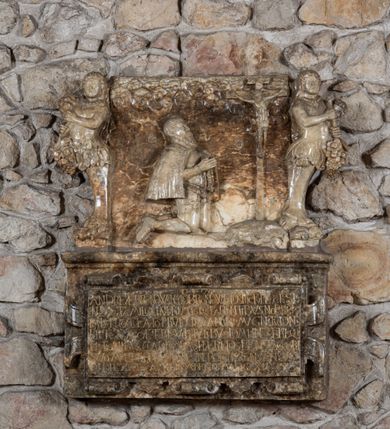 Zdjęcie nr 2: Epitafium złożone z dwóch płyt w kształcie leżącego prostokąta: u dołu płyta z inskrypcją, w obramieniu z ornamentem kartuszowo-zawijanym; ponad nią płaskorzeźbiona płyta z figuralnym przedstawieniem, flankowana dwiema groteskowymi hermami kobiet z biodrami okrytymi liśćmi akantu, stojące na grubych, lwich łapach, trzymające kiście winogron. W polu górnej płyty klęcząca postać zmarłego, ukazana z profilu, ze złożonymi w geście modlitwy rękoma, adorującego krucyfiks. W dłoniach trzyma różaniec. Twarz okala długa, spiczasta broda, wąsy oraz krótkie włosy odsłaniające prawe ucho. Przedstawiony jest w zbroi, krótkiej pelerynie przerzuconej na plecy. Ciało Chrystusa w lekkim zwisie, pochylone jest w kierunku prawego ramienia. Ponad sceną schematycznie opracowane obłoki o kształcie małżowin. Inskrypcja na dolnej płycie majuskułą po łacinie: D.O.M. / ANDREAE BRONOWSKY DE BRONOW EX DISTRICTV PLOCENSI / INSIGNI FAMILIA INPRIMIS QVE PARENTIBVS NOBILISS/IMIS PROCREATO PRVDENTIA ANIMI MAGNITVDINE / PIETATE ACCAE TERIS VIRTVTIBVS DOMIINE X TERISQVE / NATIONIBVS CLARISSIMO HAEREDES BENEFACTORI / SVO MAERENTES POSVERVNT OBIT A GENSANNVM / LVI DIE XXIX APRILIS ANNO MDCXII. Poniżej epitafium znajduje się tabliczka z informacją: „EPITAFIUM JĘDZRZEJA BRONOWSKIEGO PRZENIESIONO DO WNĘTRZA KOŚCIOŁA W 1996 R. STARANIEM PROBOSZCZA KS. CZESŁAWA PUTO I KONSERWATORA MGR DANUTY MAJEWSKIEJ ORAZ POŚWIĘCONO PONOWNIE Z UDZIAŁEM CZŁONKÓW STOWARZYSZENIA BRONOWSKICH H. KORAB.