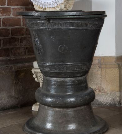 Zdjęcie nr 3: Chrzcielnica gotycka w kształcie kielicha. Posiada kolistą stopę, która przechodzi w stożkowato zwężającą się tuleję z wydatnym wałkiem w połowie wysokości. Czara dołem lekko zaokrąglona, rozchylająca się ku górze. Płaszcz dekorowany u dołu i poniżej górnej krawędzi wąskimi pasami z minuskułowymi napisami, przedzielone motywem lilii:  MARIA ROSA ROT HIS UNS, ANNO DOMINI 1462. Pomiędzy nimi rozmieszczone są na obwodzie cztery plakietki przedstawiające trójpostaciową Grupę Ukrzyżowania oraz frontalny wizerunek księcia zatorskiego Wacława w całej postaci. W prawej ręce trzyma włócznię, lewą dłoń opiera na tarczy z orłem. Twarz okala broda zakończona w szpic oraz długie i sfalowane włosy. Głowę wieńczy niewysoka książęca mitra. Ubrany jest w długi płaszcz narzucony na późnogotycka zbroję. Drewniana pokrywa chrzcielnicy została dodana wtórnie.