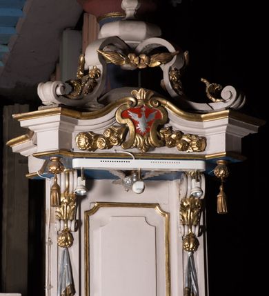 Zdjęcie nr 3: Ambona przyścienna, wisząca, z dostępem w postaci dobudowanych do kosza jednobiegowych schodów z podestem i pełną balustradą, po prawej stronie. Kosz na planie kwadratu o ściętych narożach, na cokole w formie spłaszczonego wałka, z podwieszeniem w postaci ostrosłupa o wklęsłych bokach dekorowanych liśćmi, w narożach ujętego taśmami, zakończonego szyszką. Kosz z pilastrami w narożach, których trzony przechodzą w spływy wolutowe, w partii cokołu przyjmując kształt cęgi, dekorowane są kampanulami i zwisami roślinnymi. Pilastry podtrzymują belkowanie, którego gzyms tworzy parapet kosza. Ścianki zdobione płycinami o kształcie zbliżonym do kwadratu o wklęsłych narożach, zwieńczonymi muszlami z kampanulami. Zaplecek wąski, wydłużony, flankowany lizenami zakończonymi konsolami, dekorowanymi akantem z podwieszonymi pąkami i tkaniną. W polu płycina o kształcie stojącego prostokąta o wklęsłych narożach. Baldachim na planie kwadratu o ściętych narożach, z dołączonymi w ich miejsce impostami z podwieszonymi chwostami. Na frontowej ściance zakończonej dwoma wolutowymi fragmentami gzymsu kartusz z malowanym wizerunkiem niezidentyfikowanego herbu (w czerwonym polu srebrny orzeł z gwiazdą nad głową). Na krawędzi kartusza sygle „K” i „PI”. Kartusz ujęty zwisami kwiatowymi. Na baldachimie cztery kabłąki podtrzymujące wazon, dekorowane kampanulami i ornamentem roślinnym. Na podniebieniu gołębica Ducha Świętego w glorii promienistej. Struktura polichromowana w kolorze białym, profile i ornamentyka złocone, detal srebrzony. 


