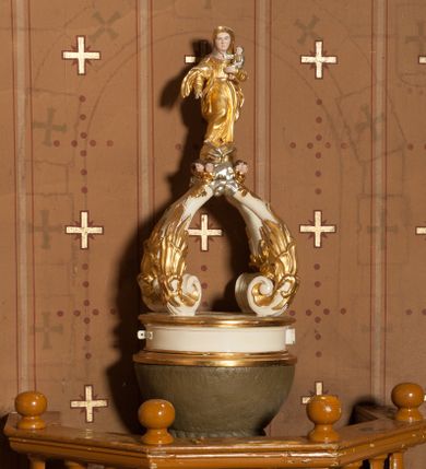 Zdjęcie nr 1: Stopa na planie koła, spłaszczona, na cokole. Trzon w formie dwulalkowej tralki, z pierścieniem w kształcie skręconego sznura pośrodku. Czara półkolista, gładka, u jej podstawy pierścień w kształcie skręconego sznura. Pokrywa drewniana, na planie koła, w formie cokołu z czterema wolutami dekorowanymi rocaille'em, tworzącymi podstawę dla figurki Matki Boskiej Niepokalanie Poczętej. Maria ukazana frontalnie, w kontrapoście, stoi na globie, posadowionym na obłokach z uskrzydlonymi główkami anielskimi. Lewą ręką podtrzymuje Dzieciątko, prawą wyciąga w przód, prawą stopą depcze węża. Twarz ma okrągłą, o schematycznie zaznaczonych rysach. Ubrana jest w suknię przylegającą do ciała, przepasaną w talii oraz płaszcz zawiązany na prawym ramieniu, na głowie ma welon. Pokrywa polichromowana w kolorze białym, ornamentyka i strój Marii złocony, detal srebrzony, elementy anatomiczne malowane naturalistycznie. 



