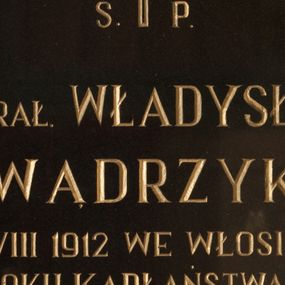 Zdjęcie nr 1: Płyta granitowa w formie prostokąta zbliżonego do kwadratu, w drewnianej, profilowanej ramie, polichromowanej na czarno. W polu złocona inskrypcją: „Ś(więtej) P(amięci) / KS(IĄDZ) PRAŁ(AT) WŁADYSŁAW / WĄDRZYK / UR(ODZONY) 11 VIII 1912 WE WŁOSIENICY / ZM(ARŁ) W 51 ROKU KAPŁAŃSTWA 13 XI 1990 / WICEDZIEKAN DEKANATU MAKOWSKIEGO / PROBOSZCZ W ZAWOI W LAT(ACH) 1957 – 1987 / GORLIWY I ODDANY APOSTOŁ SŁOWA / BOŻEGO. / Na wieczną pamiątkę Bogu wdzięczni / za okazaną miłość i dobroć / Parafianie.”