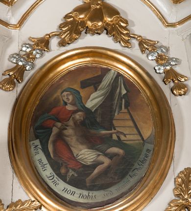 Zdjęcie nr 2: Obraz w formie stojącego owalu. Na pierwszym planie Matka Boska ukazana frontalnie, w pozycji siedzącej, z głową skierowaną w prawo, obiema rękami podtrzymuje leżące na jej kolanach martwe ciało Chrystusa. Lewą ręką trzyma jego przedramię, prawą bark. Twarz ma owalną, o wąskich oczach, prostym nosie, małych ustach. Ubrana jest w czerwoną suknię i niebieski płaszcz zarzucony na głowę i ramiona. Chrystus ukazany w pozycji siedzącej, oparty o Marię, z głową opadającą na lewy bark, z wyciągniętą lewą ręką oraz ugiętymi nogami. Twarz ma szczupłą, o zamkniętych oczach, dużym nosie i małych ustach, okoloną krótką brodą i włosami sięgającymi ramion. Ciało ma szczupłe, poranione, z dużą raną w prawym boku, na dłoniach i stopach. Przez biodra ma przewiązane białe, krótkie perizonium. Przy nodze Marii znajduje się dzbanek i tabliczka z napisem „I.N.R.I”. Scena ukazana na tle pejzażu z widocznym krzyżem, z zawieszoną na nim białą tkaniną oraz opartą drabiną. Wzdłuż dolnej krawędzi obrazu biała banderola z napisem „Non nobis D(omi)ne non nobis. sed nomini tuo da Gloriam”. 


