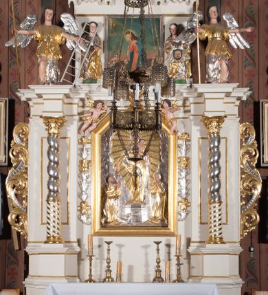 Zdjęcie nr 4: Nastawa architektoniczna, jednokondygnacyjna ze zwieńczeniem, ustawiona na dwustrefowym cokole, w górnej strefie z wyłamanymi, zdwojonymi prostopadłościanami. Ołtarz drewniany, prostopadłościenny, z drewnianą mensą. Antepedium ujęte profilowaną ramą, w polu na pomarańczowym tle namalowana korona otwarta z różańcem nad symetrycznie umieszczonymi liśćmi, z napisem „Królowo różańca świętego módl się za nami”. Nastawa ujęta parą kolumn o skręconych trzonach podzielonych na dwie strefy i kapitelach kompozytowych, ustawionych na tle wyłamanych ścianek bocznych nastawy. Podpory dźwigają pełne belkowanie, częściowo przerwane nad polem środkowym, wyłamane na ich osi. Na belkowaniu ustawione figury aniołów z arma Christi. Pole centralne wypełnione wnęką w formie stojącego prostokąta o ściętych górnych narożach, ujęte profilowaną ramą, z płaskorzeźbą Matki Boskiej Różańcowej. Wnęka flankowana ornamentem roślinnym, w przyłuczach dwa putta. Kondygnacja ujęta uszami utworzonymi z akantu i wstęgi. Zwieńczenie w formie leżącego prostokąta. W polu obraz Chrystusa w Ogrójcu o kształcie zbliżonym do kwadratu, ujęty profilowaną ramą. Obraz flankują figury św. Marii Magdaleny i św. Weroniki, nad którymi znajdują się baldachimy ze stylizowanym lambrekinem. Całość zwieńczona płaskorzeźbą tronującego Boga Ojca pośród obłoków i uskrzydlonych główek anielskich, w glorii promienistej. Struktura polichromowana w kolorze białym, profile złocone, kolumny, ornamentyka złocone i srebrzone. 


